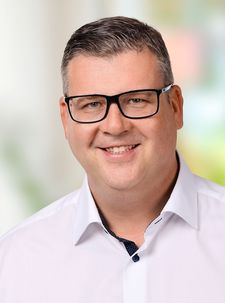 Porträt eines lächelnden Mannes mit schwarzer Brille und weißem Hemd