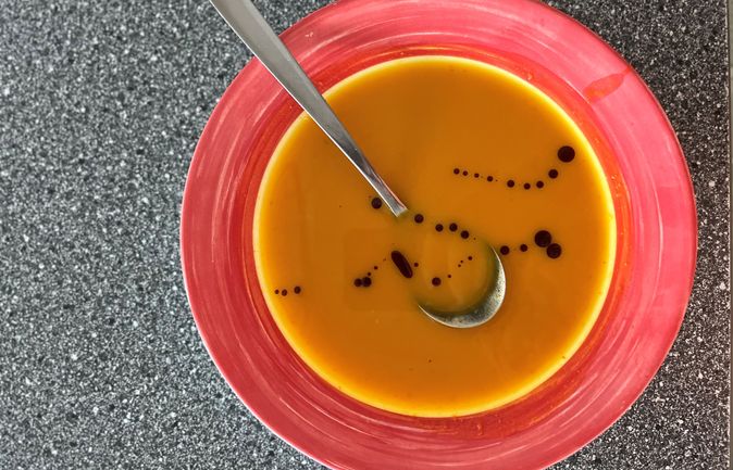 Rote Schale mit orangener Suppe, Löffel und dunklen Öltropfen