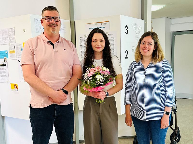 Drei Mitarbeitende des Sozialdienstes, mittlere Person mit Blumenstrauß