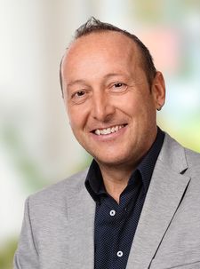 Lächelnder Mann mittleren Alters mit Ohrring und grauem Sakko
