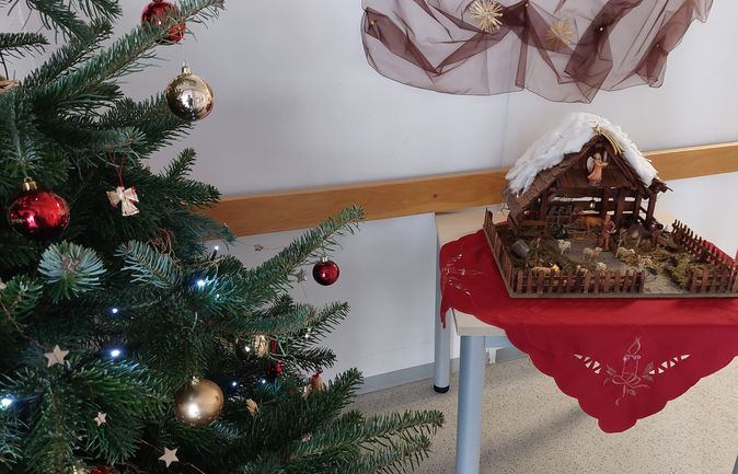 Weihnachtsbaum mit roten und goldenen Kugeln neben einer Krippe auf einem Tisch