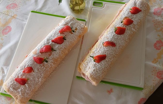 Zwei Erdbeerrouladen mit Puderzucker auf Tisch neben Vase mit Pfingstrosen