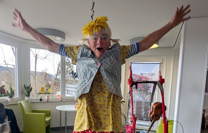 Clown mit gelber Blume im Haar springt mit ausgebreiteten Armen