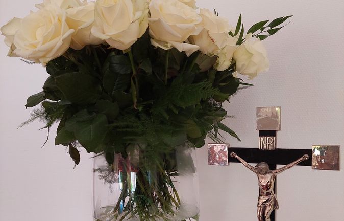 Weißer Rosenstrauß in Vase neben Kruzifix bei Gedenkfeier