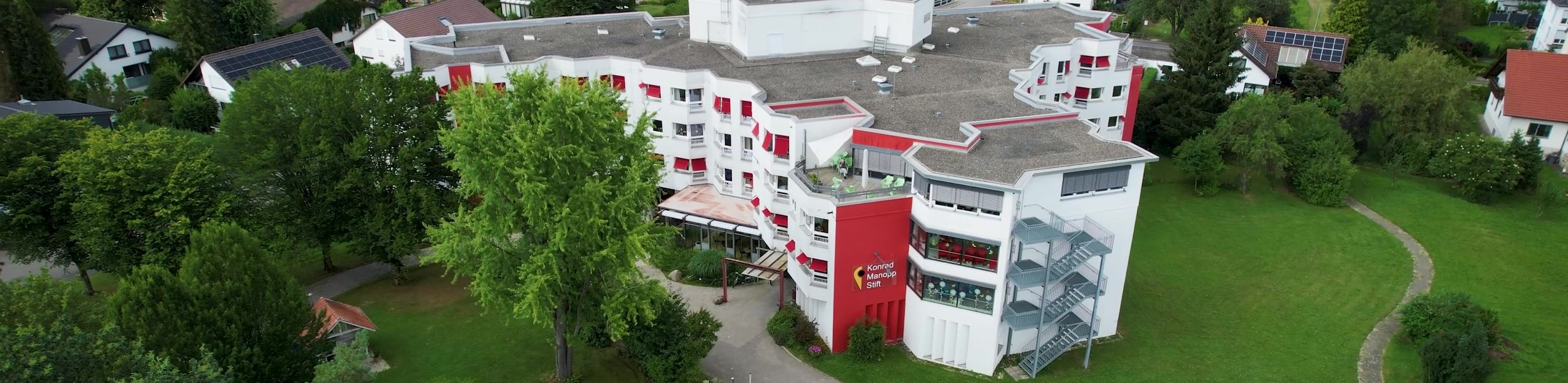 Luftaufnahme eines großen weißen Wohngebäudes mit roten Akzenten in grüner Wohnumgebung