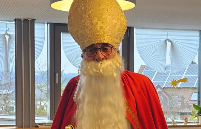 Person als Nikolaus mit Mitra rotem Mantel weißem Bart und Buch