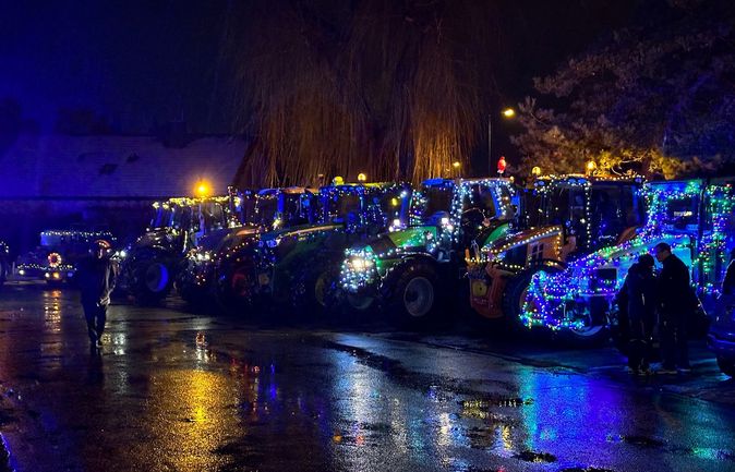 Reihe weihnachtlich beleuchteter Traktoren bei Nacht auf nasser Straße