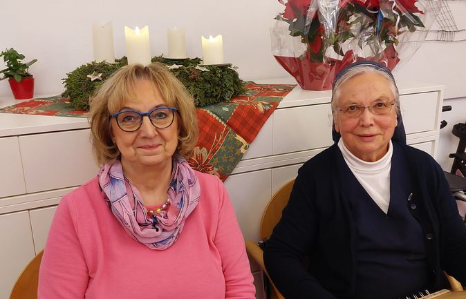 Zwei ältere Frauen vor Adventskranz, Kerzen, Weihnachtsstern und Saiteninstrument