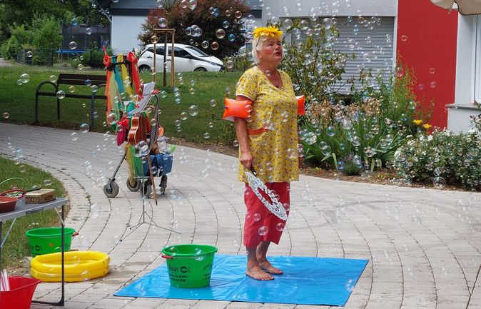 Clown mit Sonnenblumenkranz erzeugt Seifenblasen für Bewohner