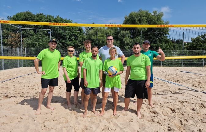 Team KoMa-Stift in grünen Trikots auf Beachvolleyballfeld beim Keppler-Cup