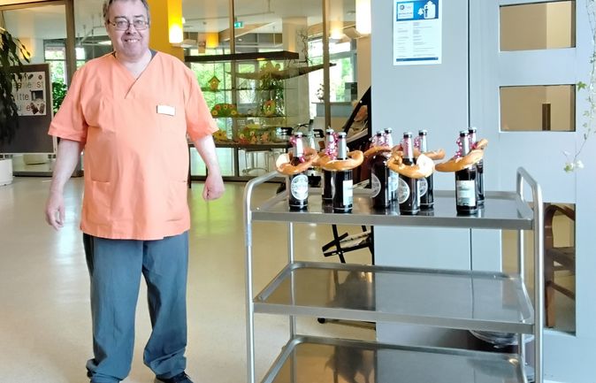Mann in orange Arbeitskleidung neben Servierwagen mit Bierflaschen und Brezeln zum Vatertag
