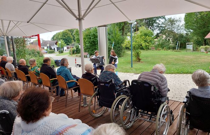 Zwei Akkordeonspielende unter Sonnenschirmen vor älteren Zuhörenden