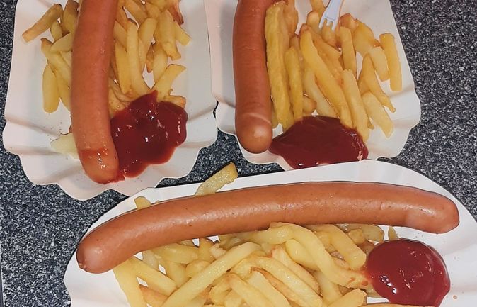 drei Portionen Pommes mit Würstchen und Ketchup in Papierschalen