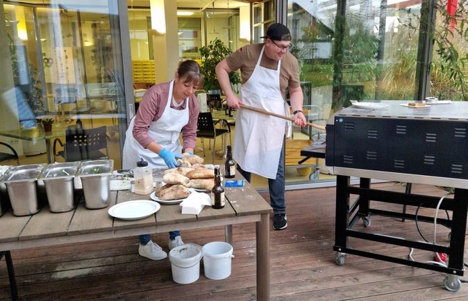 Zwei Mitarbeitende bereiten Brot am Grillofen beim Fest im Konrad-Manopp-Stift