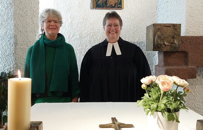 Pfarrerin neben Gemeindemitglied vor Altar mit Kerzen und Blumen